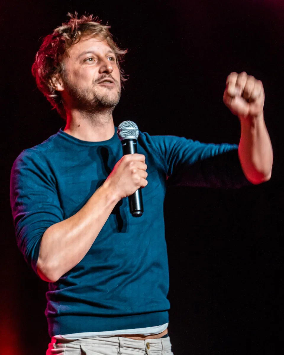 Yvain sur scène, micro à la main et poing levé, sous une lumière rouge.